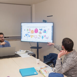 Professor e aluno em uma sala de aula, com uma televisão ao fundo