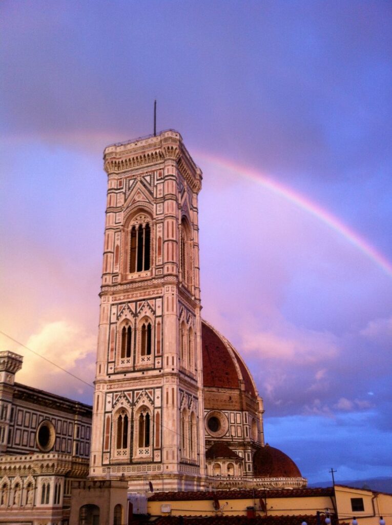 Torre histórica em Florença com arco-íris ao fundo.