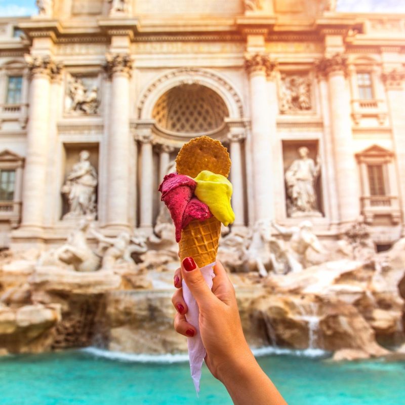 Mão segurando um gelatto diante da Fontana di Trevi em Roma.