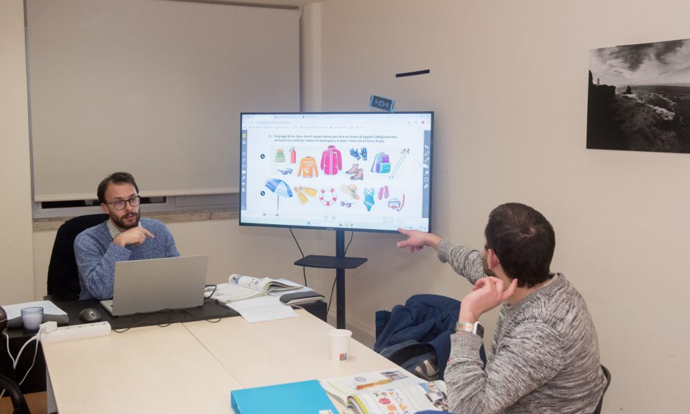 Professor e aluno em uma sala de aula, com uma televisão ao fundo
